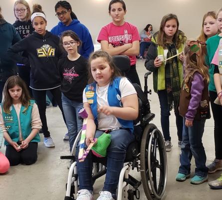 Girl in a wheelchair testing a catapult, a group of girls watches behind her