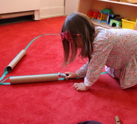 Young girl pushes a matchbox car over a paper towel roll