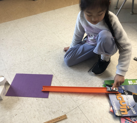 A girl holding a matchbox car at the top of a ramp