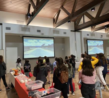 Group of girls watching a video on a large screen. The screen says, "Reminding women they have no limits"