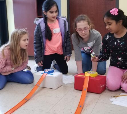 Four girls looking at a matchbox car with two tracks on the floor