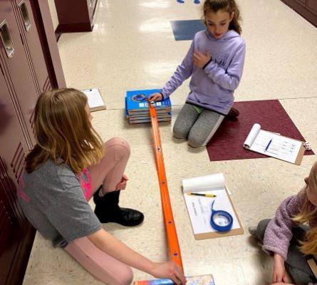 Three girls sitting on the floor next to an orange matchbox car track