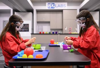 Two girls in safety goggles and red lab coats
