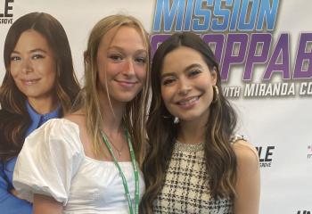 Morgan S and Miranda Cosgrove - two young women standing in front of a Mission Unstoppable tv show banner
