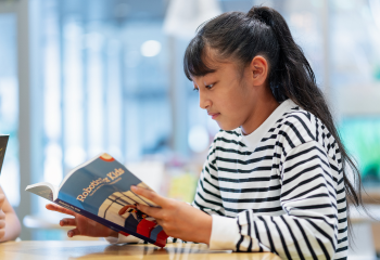 Girl wearing striped shirt, reading a book at a table