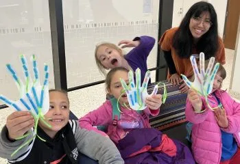 Group of children holding up paper hands with adult smiling at the camera