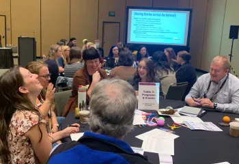 Groups of adults talking at round tables with a screen in the background