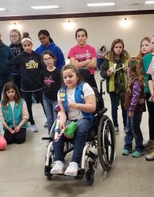Girl in a wheelchair testing a catapult, a group of girls watches behind her