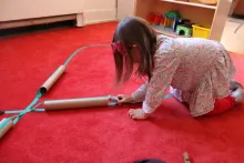 Young girl pushes a matchbox car over a paper towel roll