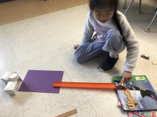 A girl holding a matchbox car at the top of a ramp