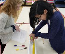 Two girls measuring matchbox car on a track