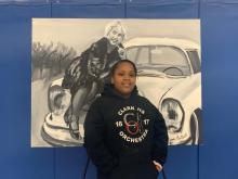 Girl standing in front of a black and white painting of a woman sitting on the hood of a car