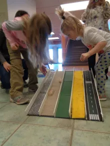 Two girls test cars on a ramp with different surfaces