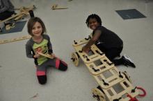 Two girls building a large car with wooden pieces from a rig a ma jig set