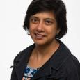 woman with short, dark hair, wearing denim jacket and multi-colored shirt