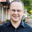 Brian Weisfeld - photo of man with short hair and glasses wearing black collared shirt