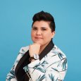 Person with short dark hair in front of a blue background