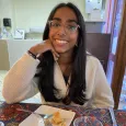 Teen girl with glasses and long dark hair sitting at a table with a plate in front of her