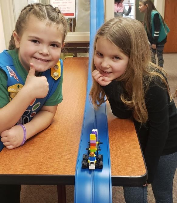 Two girls next to blue matchbox car track