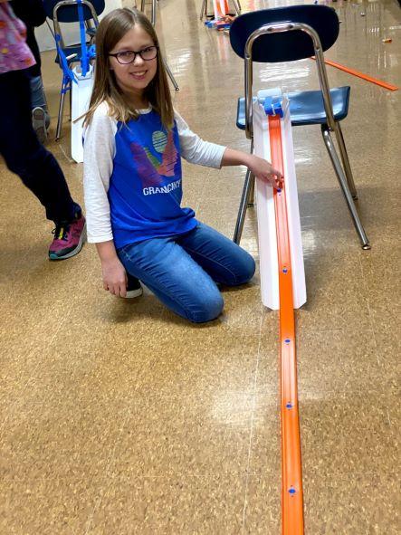 Girl sitting on the floor next to an orange matchbox track propped up on a chair