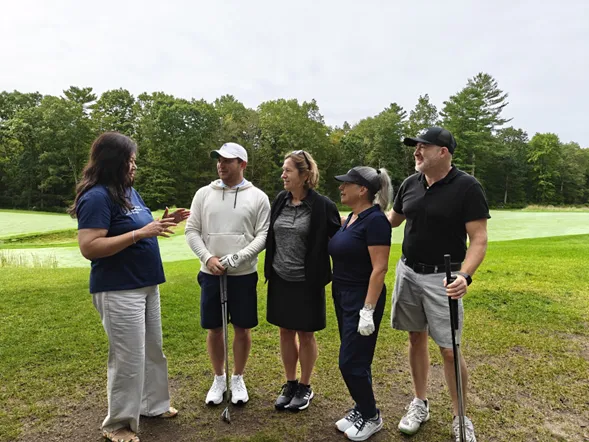 Woman talks with four people in golf attire on a golf course